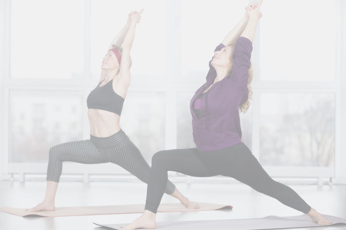 Two women in a yoga studio keep their lower back safe in yoga by practicing warrior one pose.