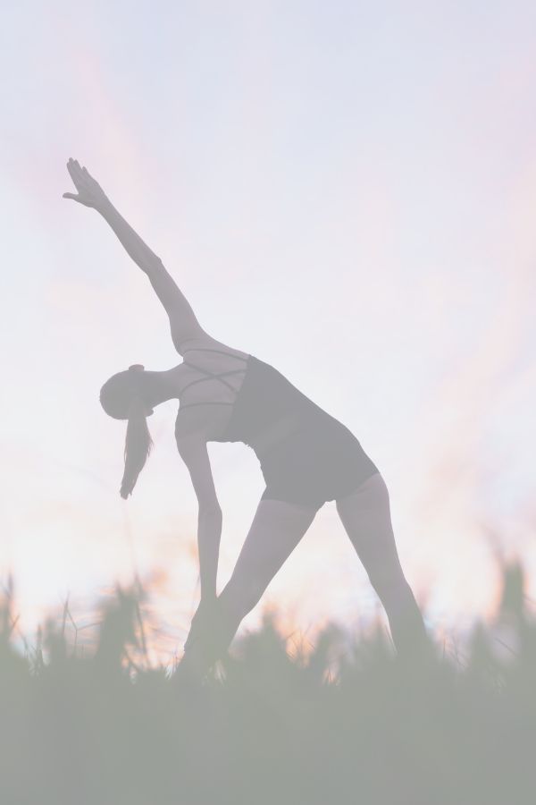 A woman is practising yoga in a field. She is silhouetted against the purple and orange sunset.