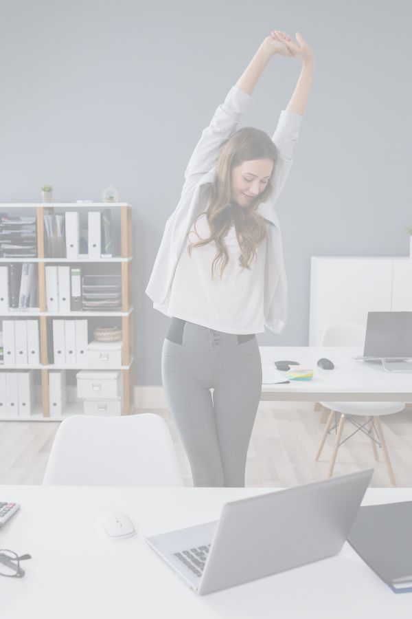 A woman is standing at a desk in an office performing a side bend stretch.