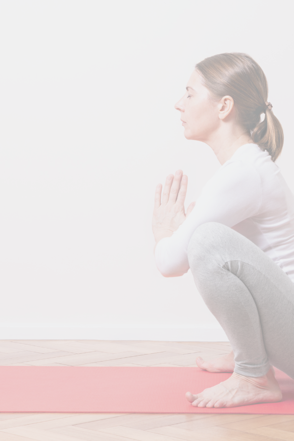 A woman is side on to the camera in a deep yoga squat with her hands in prayer position.