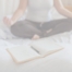 A woman is sitting on her bed contemplating the yoga journal prompts in her open notebook.