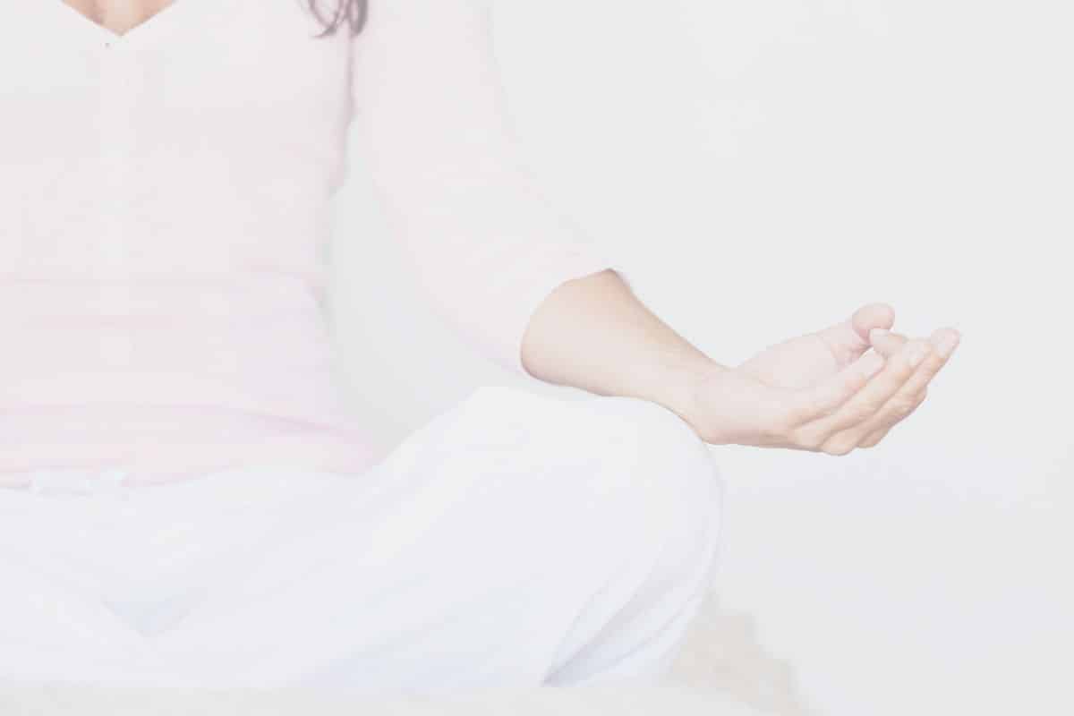 A woman in a light pink top and white pants is meditating using meditation intention examples.