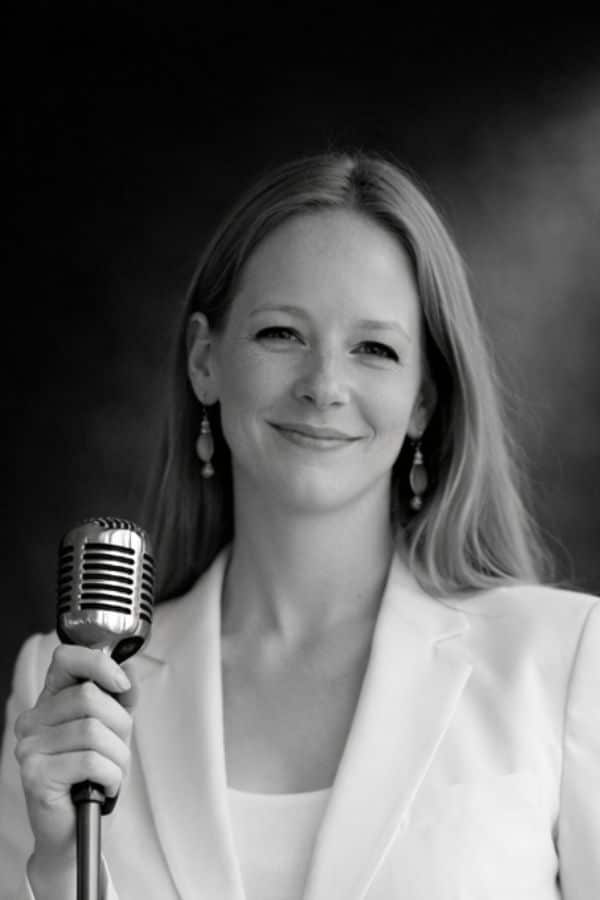 Ellie Smith Public Speaking Coach Ellie Smith is standing smiling behind a vintage microphone